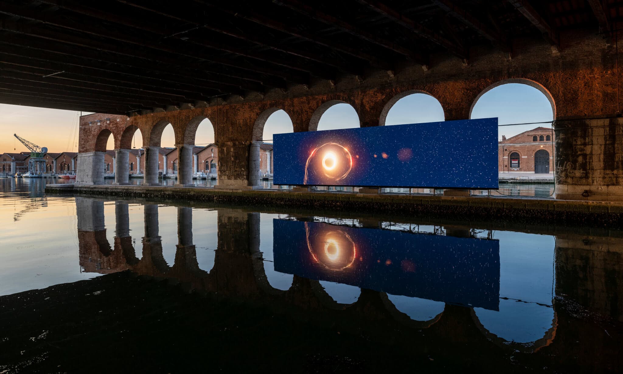 A work of art hangs in front of a body of water and a scene of arches.